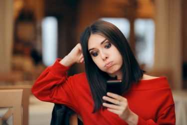 Egy fiatal nő munkaidőn kívül telefonját nézi, bizonytalan arckifejezéssel.