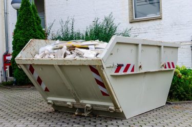 Konténerben gyűjtött bontási és építési törmelék egy épület mellett.