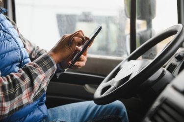 Teherautó-sofőr használ mobileszközt a jármű fülkéjében, digitális munkakörnyezetben.