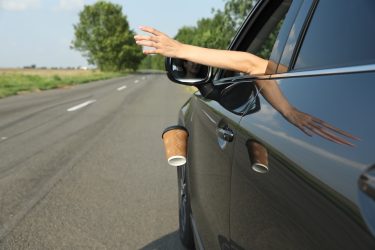 Az autó ablakából kilógó kéz és egy eldobott papírpohár az útmenti szemetelés problémáját jeleníti meg.