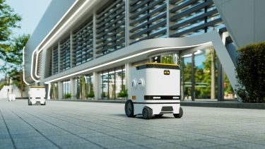 Autonóm kiszállító robot halad egy modern városi környezetben, miközben csomagokat szállít.
