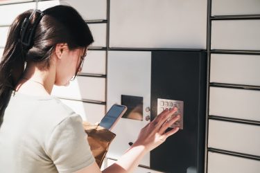 Egy vásárló csomagot vesz át csomagautomatából mobiltelefon segítségével.